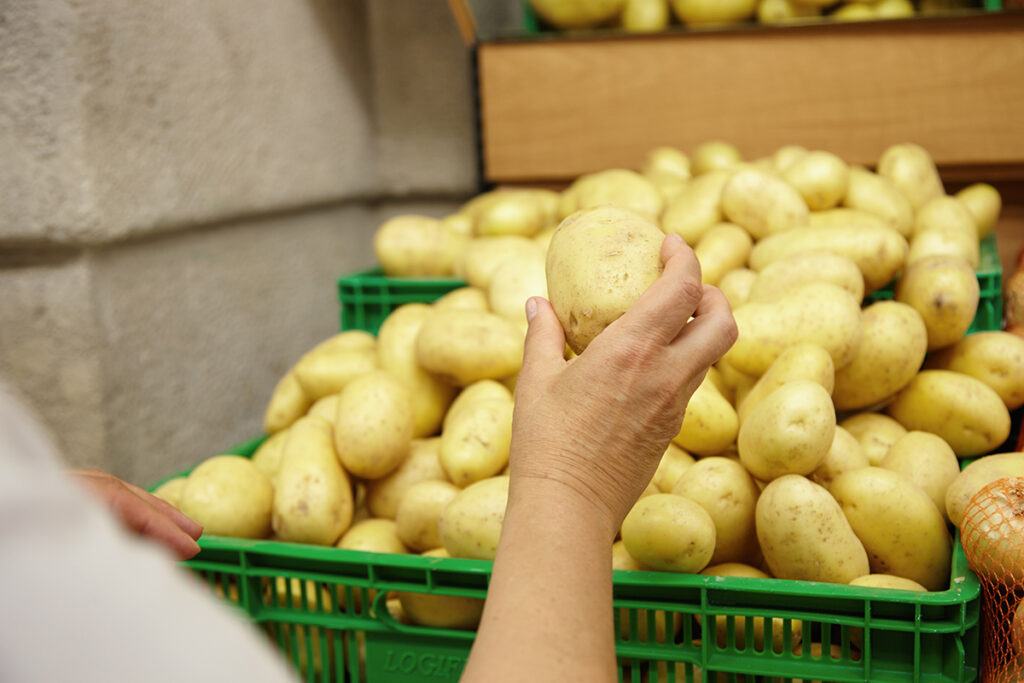 podrezannyi portret starsei kavkazskoi zensiny protagivaa ruku s bol soi kartoskoi v nei gotovyi polozit ee v svou korzinu delaa pokupki v supermarkete isa ovosi dla prigotovlenia semeinogo uzina