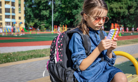 ucenica nacal noi skoly s rukzakom ispol zuet smartfon sida vozle skoly