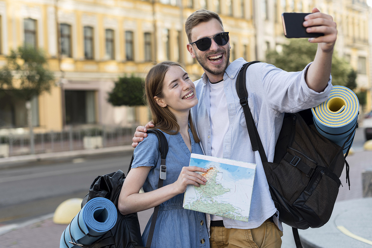 smiley tourist couple taking selfie while carrying backpacks