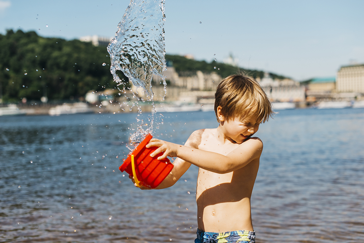 young boy spills water from bucket sea beach