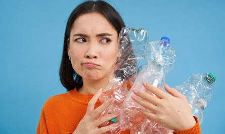 annoyed korean woman looking with blaming face holding plastic bottles standing blue studio bac