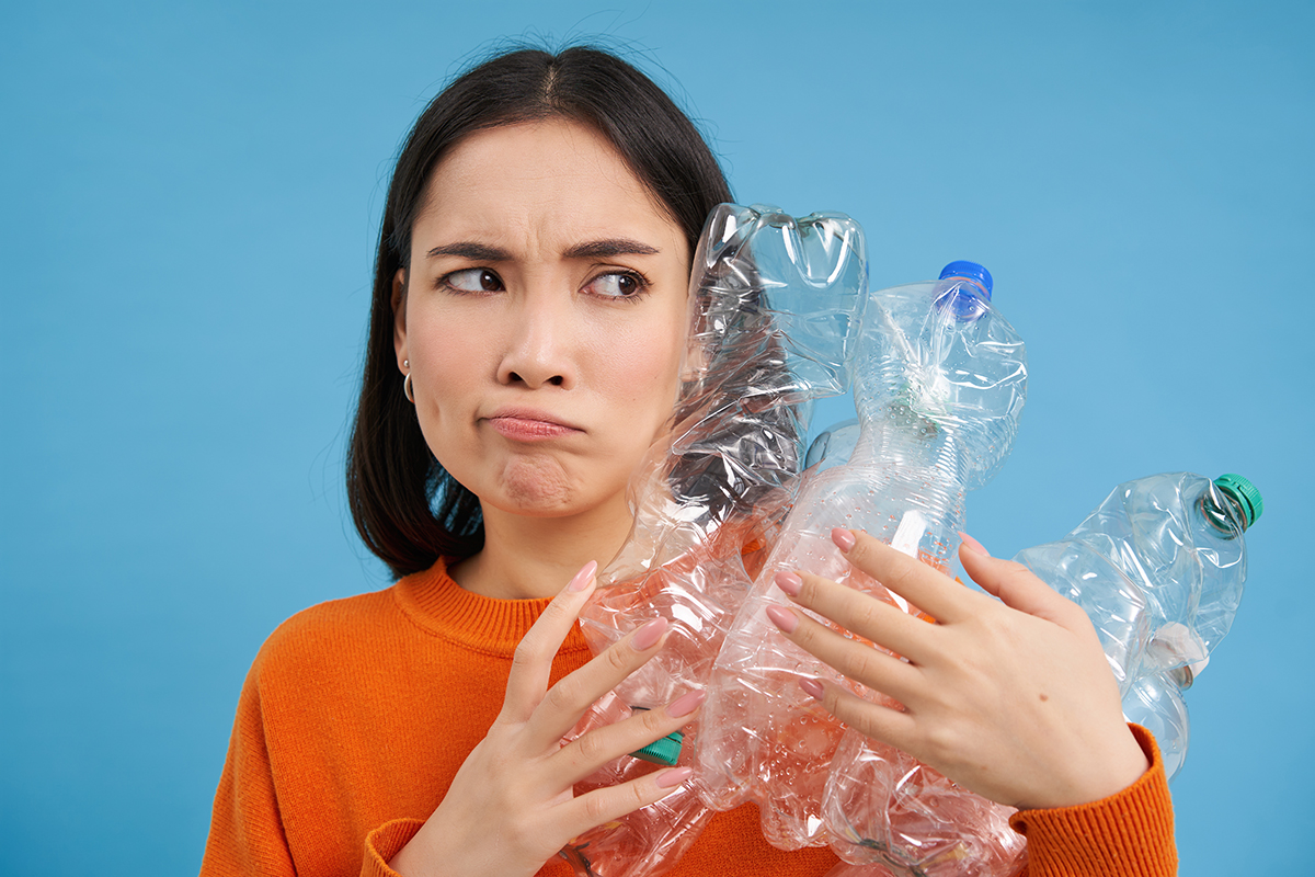 annoyed korean woman looking with blaming face holding plastic bottles standing blue studio bac