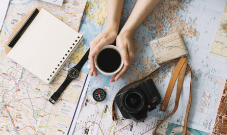 hand holding coffee cup map surrounded with spiral notepad compass wristwatch camera strap 1