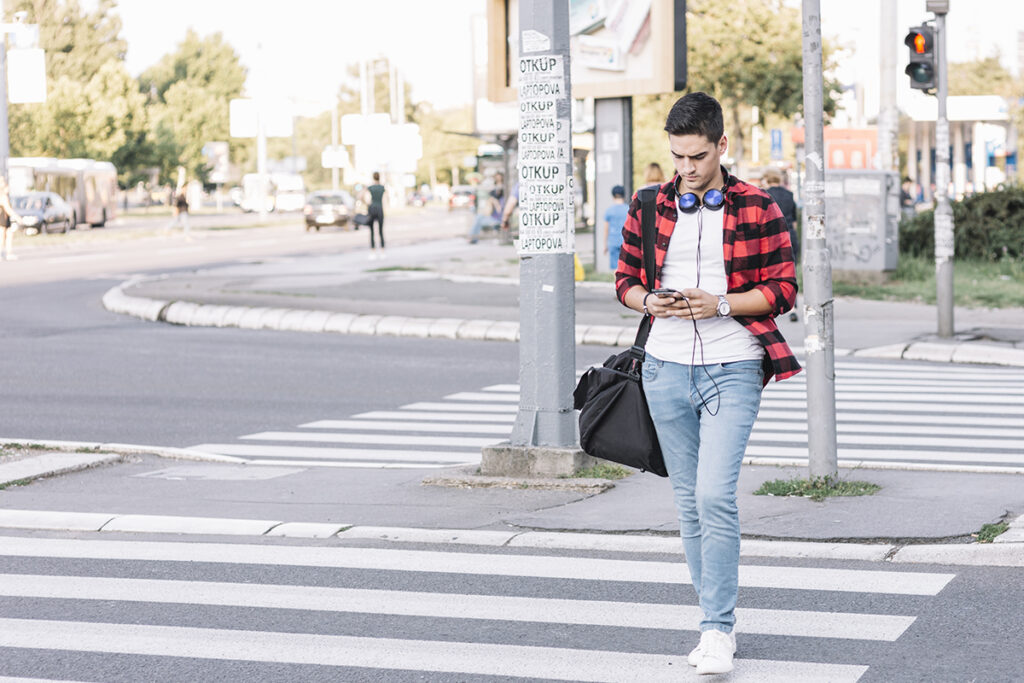 young man with smartphone crossing street