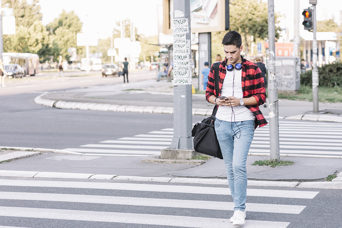 young man with smartphone crossing street