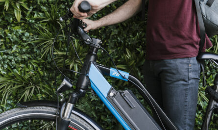 close up sideways cyclist holding e bike with green wall background