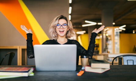 funny happy excited young pretty woman sitting table black shirt working laptop co working office wearing glasses