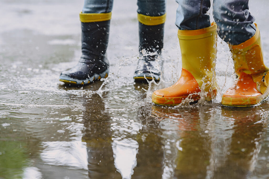 funny kids rain boots playing with paper ship by puddle
