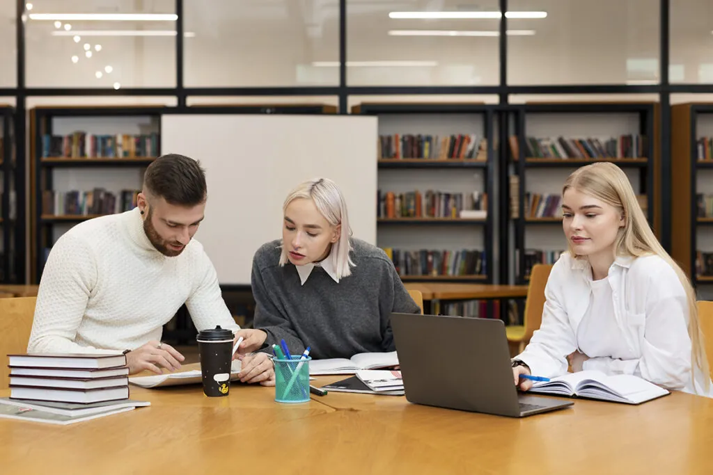 three friends studying from documents laptop library